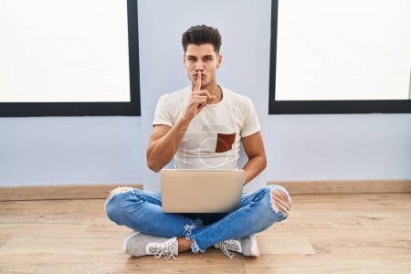 Foto de Joven hispano usando laptop en casa pidiendo estar callado con el dedo en los labios. silencio y concepto secreto. - Imagen libre de derechos