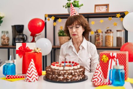 Photo for Middle age woman celebrating birthday holding big chocolate cake thinking attitude and sober expression looking self confident - Royalty Free Image