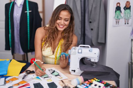 Téléchargez les photos : Jeune belle hispanique femme tailleur dessin vêtements conception tenant tissu à tailleur boutique - en image libre de droit