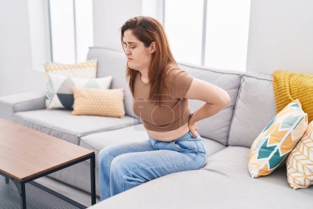 Foto de Mujer joven que sufre de dolor de espalda sentada en el sofá en casa - Imagen libre de derechos