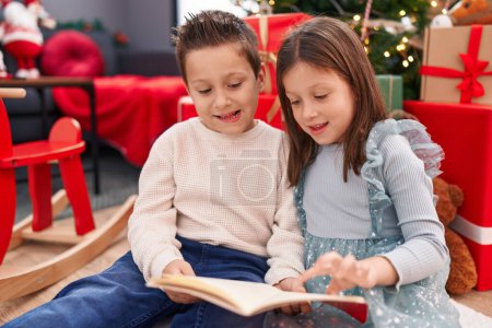 Photo for Adorable boy and girl reading book celebrating christmas at home - Royalty Free Image