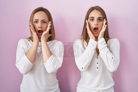 Photo for Middle age mother and young daughter standing over pink background afraid and shocked, surprise and amazed expression with hands on face - Royalty Free Image