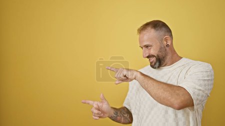 Photo for Attractive young man confidently pointing with a bright smile on his face. standing against an isolated yellow background with copy space. presentation of joy and positivity. - Royalty Free Image