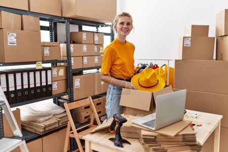Téléchargez les photos : Jeune femme blonde ecommerce travailleur d'affaires chapeau d'emballage sur boîte en carton au bureau - en image libre de droit