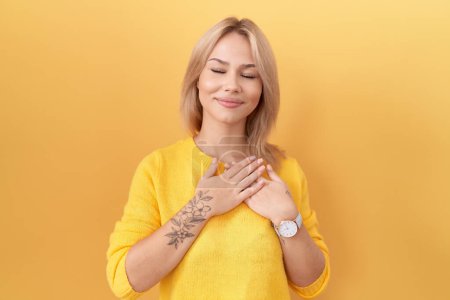 Téléchargez les photos : Jeune femme caucasienne portant un pull jaune souriant avec les mains sur la poitrine avec les yeux fermés et geste reconnaissant sur le visage. concept de santé. - en image libre de droit