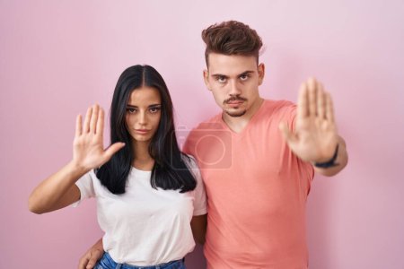Téléchargez les photos : Young hispanic couple standing over pink background doing stop sing with palm of the hand. warning expression with negative and serious gesture on the face. - en image libre de droit