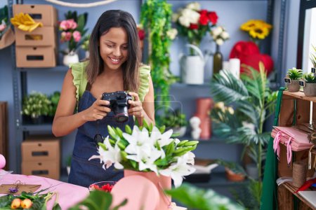 Foto de Joven florista hispana sonriendo confiada hacer foto por cámara en floristería - Imagen libre de derechos