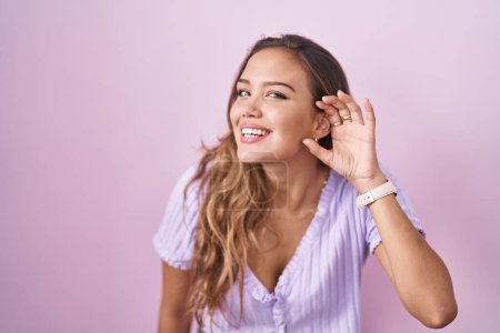 Téléchargez les photos : Jeune femme hispanique debout sur fond rose souriant avec la main sur l'oreille en écoutant une rumeur ou des commérages. concept de surdité. - en image libre de droit