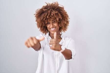 Foto de Mujer hispana joven con el pelo rizado de pie sobre fondo blanco aprobando hacer gesto positivo con la mano, pulgares hacia arriba sonriendo y feliz por el éxito. gesto ganador. - Imagen libre de derechos