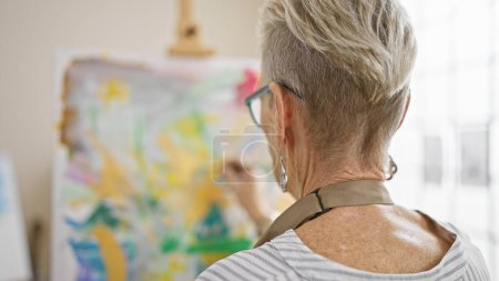 Téléchargez les photos : Femme artiste mature aux cheveux gris dessinant passionnément vers l'arrière, perdue dans son univers de créativité dans son confortable studio d'art. - en image libre de droit