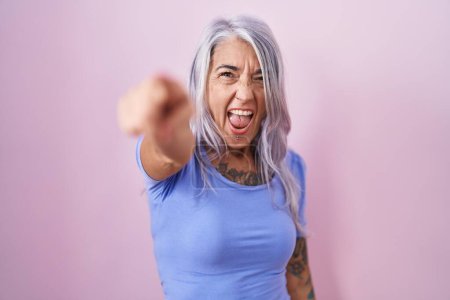 Photo for Middle age woman with tattoos standing over pink background pointing displeased and frustrated to the camera, angry and furious with you - Royalty Free Image