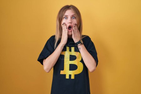 Téléchargez les photos : Blonde femme caucasienne portant Bitcoin t-shirt peur et choqué, surprise et expression étonnante avec les mains sur le visage - en image libre de droit