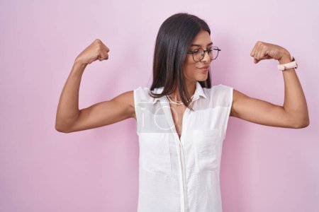 Photo for Brunette young woman standing over pink background wearing glasses showing arms muscles smiling proud. fitness concept. - Royalty Free Image