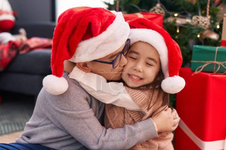 Téléchargez les photos : Frère et sœur s'embrassant et s'embrassant assis sur le sol par des cadeaux de Noël à la maison - en image libre de droit