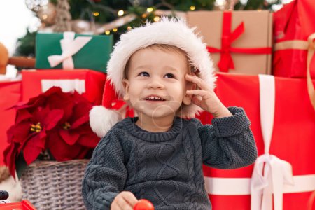Foto de Adorable niño rubio sonriendo confiado sentado en el suelo por los regalos de Navidad en casa - Imagen libre de derechos