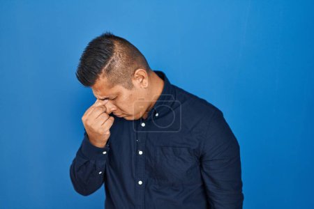 Photo for Hispanic young man standing over blue background tired rubbing nose and eyes feeling fatigue and headache. stress and frustration concept. - Royalty Free Image