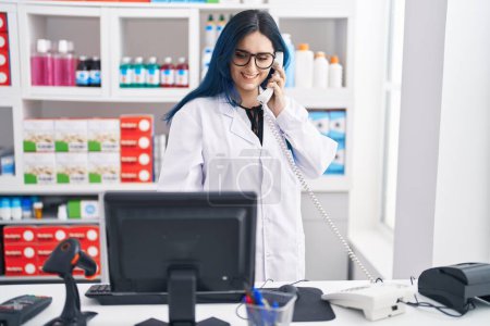Photo for Young caucasian woman pharmacist talking on telephone using computer at pharmacy - Royalty Free Image