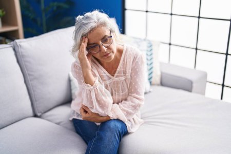 Foto de Mujer de pelo gris de mediana edad estresada sentada en el sofá en casa - Imagen libre de derechos