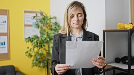Téléchargez les photos : Jeune femme blonde travailleuse d'affaires lisant le document au bureau - en image libre de droit