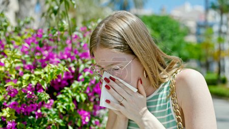 Foto de Mujer rubia joven estornudando por alergia en el parque - Imagen libre de derechos
