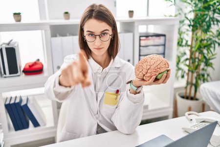 Photo for Young caucasian doctor woman holding brain as mental health concept pointing with finger to the camera and to you, confident gesture looking serious - Royalty Free Image