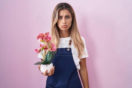 Photo for Young blonde woman wearing gardener apron holding plant depressed and worry for distress, crying angry and afraid. sad expression. - Royalty Free Image