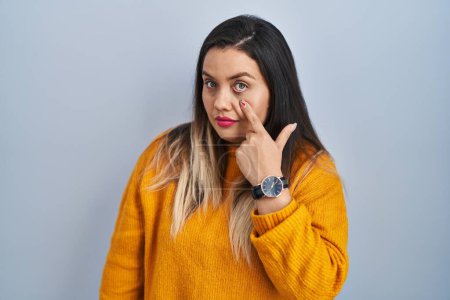Photo for Young hispanic woman standing over isolated background pointing to the eye watching you gesture, suspicious expression - Royalty Free Image