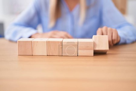 Téléchargez les photos : Jeune femme blonde femme d'affaires assise sur la table avec des cubes en bois au bureau - en image libre de droit