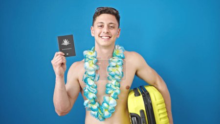 Téléchargez les photos : Jeune homme hispanique touriste tenant passeport australien et valise sur fond bleu isolé - en image libre de droit
