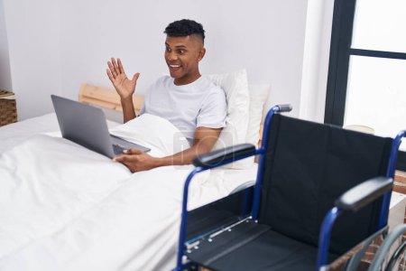 Photo for Young hispanic man lying on the bed, using wheelchair celebrating achievement with happy smile and winner expression with raised hand - Royalty Free Image