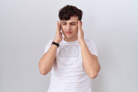 Téléchargez les photos : Jeune homme non binaire portant un t-shirt blanc décontracté avec la main sur la tête, maux de tête parce que le stress. migraine souffrant. - en image libre de droit