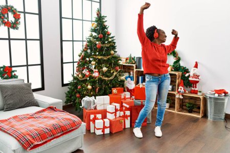 Téléchargez les photos : Femme afro-américaine écoutant de la musique et dansant debout près de l'arbre de Noël à la maison - en image libre de droit