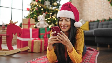 Foto de Joven mujer hispana hermosa celebrando la Navidad con el teléfono inteligente en casa - Imagen libre de derechos