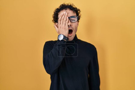 Photo for Hispanic man standing over yellow background yawning tired covering half face, eye and mouth with hand. face hurts in pain. - Royalty Free Image