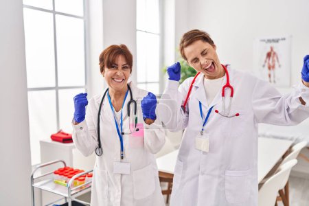 Téléchargez les photos : Deux femmes portant l'uniforme de médecin et stéthoscope très heureux et excité faisant geste gagnant avec les bras levés, souriant et criant pour le succès. concept de célébration. - en image libre de droit
