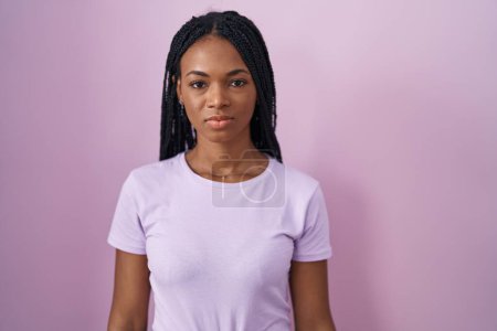 Photo for African american woman with braids standing over pink background relaxed with serious expression on face. simple and natural looking at the camera. - Royalty Free Image