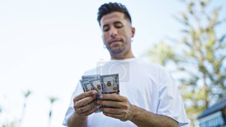 Téléchargez les photos : Young hispanic man counting dollars at street - en image libre de droit