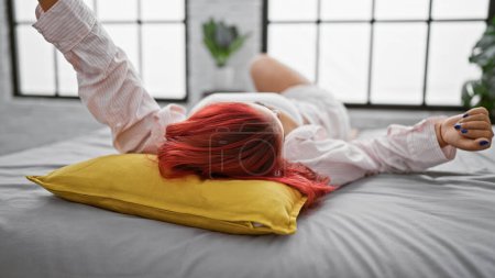 Téléchargez les photos : Réveillée et étirée, la jeune rousse profite d'une matinée détendue dans une chambre confortable, couchée confortablement sur le lit - en image libre de droit