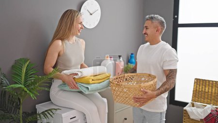 Foto de Hombre y mujer pareja poniendo toallas dobladas en la cesta en la sala de lavandería - Imagen libre de derechos