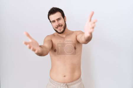 Téléchargez les photos : Jeune homme hispanique debout torse nu sur fond blanc regardant la caméra souriant à bras ouverts pour un câlin. expression joyeuse embrassant le bonheur. - en image libre de droit