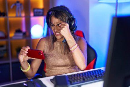 Téléchargez les photos : Jeune femme hispanique jouant à des jeux vidéo avec smartphone agacé et frustré criant de colère, criant fou de colère et la main levée - en image libre de droit
