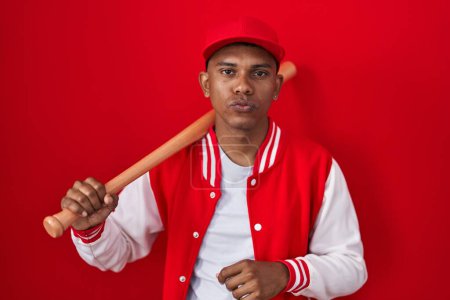 Photo for Young hispanic man playing baseball holding bat looking at the camera blowing a kiss on air being lovely and sexy. love expression. - Royalty Free Image