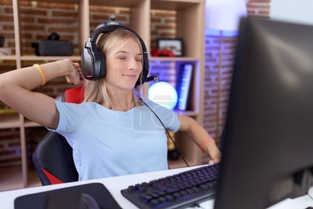 Téléchargez les photos : Jeune femme caucasienne jouant à des jeux vidéo portant des écouteurs étirant le dos, fatigué et détendu, endormi et bâillant tôt le matin - en image libre de droit