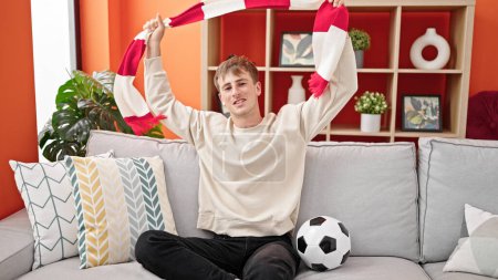 Photo for Young caucasian man supporting soccer team holding scarf at home - Royalty Free Image