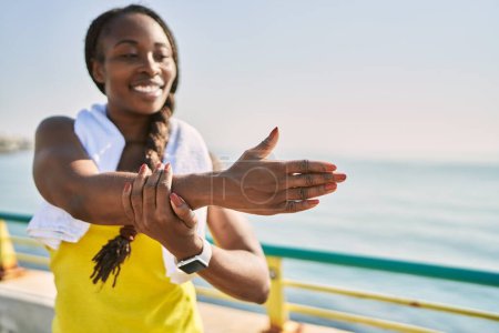 Foto de Mujer afroamericana usando ropa deportiva estirando el brazo a la orilla del mar - Imagen libre de derechos