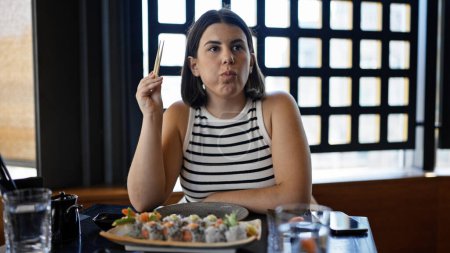 Foto de Joven mujer hispana hermosa comiendo sushi en el restaurante - Imagen libre de derechos