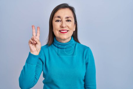 Téléchargez les photos : Moyen Age femme hispanique debout sur fond isolé montrant et pointant vers le haut avec les doigts numéro deux tout en souriant confiant et heureux. - en image libre de droit