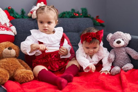 Téléchargez les photos : Adorables filles assises sur le canapé célébrant Noël à la maison - en image libre de droit