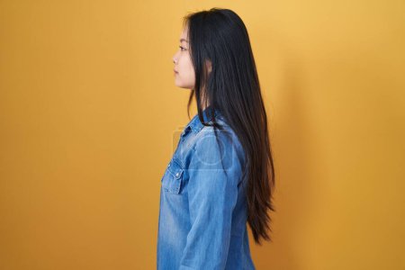Téléchargez les photos : Jeune femme asiatique debout sur fond jaune regardant vers le côté, pose de profil relax avec le visage naturel et sourire confiant. - en image libre de droit