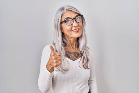 Photo for Middle age woman with grey hair standing over white background doing happy thumbs up gesture with hand. approving expression looking at the camera showing success. - Royalty Free Image